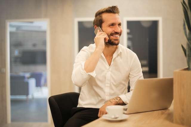 A man talking on phone in front of a laptop