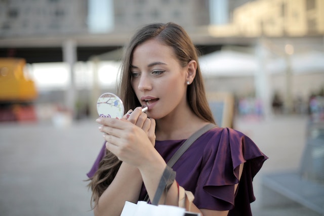 A person doing up her lipstick while looking at her compact