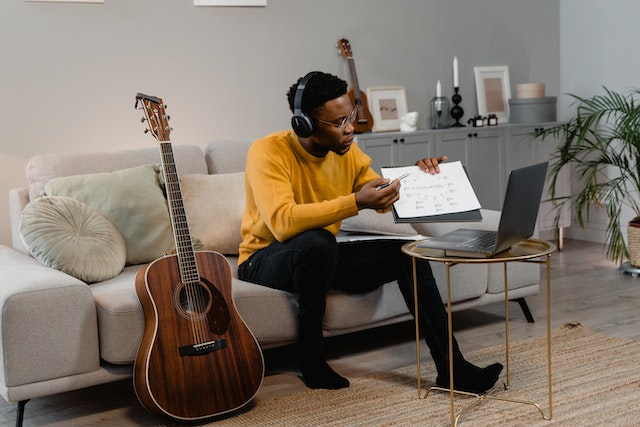 A black man teaching guitar through music sheets on a laptop