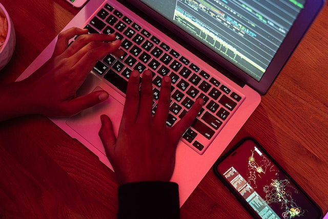 Photo of a person coding with a laptop and a smartphone