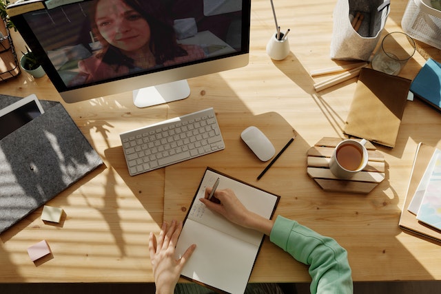 A person taking notes in front of a laptop