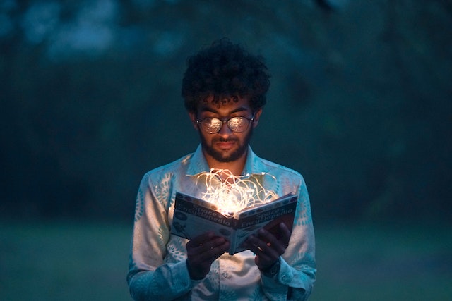Man staring at a book lit up by fairy lights