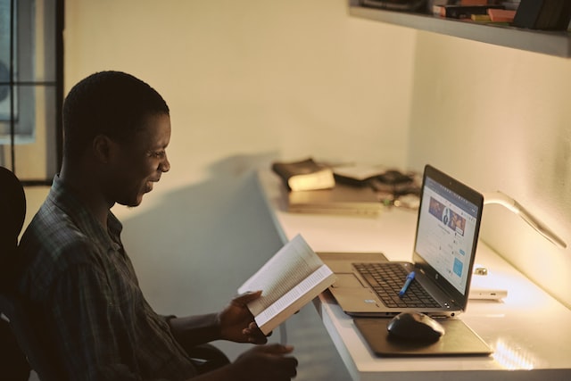 Person reading a book in front of laptop